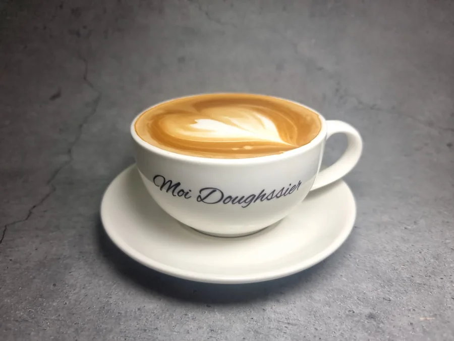 A freshly made latte in a branded Moi Doughssier cup with latte art, served at the café